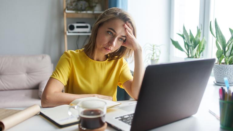 A woman working at her laptop with her head resting in her hand